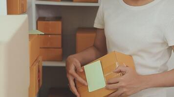 joven y atractiva mujer asiática propietaria de un negocio de inicio mira el trabajo de la cámara feliz con la caja en casa prepara la entrega de paquetes en la cadena de suministro de pymes, adquisiciones, omnicanal o concepto de cuarentena de coronavirus. video