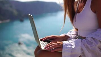 freelance, digital nômade. bem olhando meio envelhecido mulher digitando em computador portátil teclado ao ar livre em terraço com lindo mar visualizar. fechar acima mulher mãos escrevendo em computador. viagem e feriados conceito. video