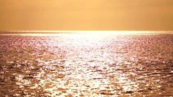 astratto mare estate oceano tramonto natura sfondo. suono di piccolo onde su d'oro acqua superficie nel movimento sfocatura con d'oro bokeh luci a partire dal sole. vacanza, vacanza e ricreativo concetto. video