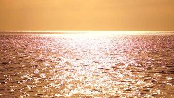 abstract zee zomer oceaan zonsondergang natuur achtergrond. geluid van klein golven Aan gouden water oppervlakte in beweging vervagen met gouden bokeh lichten van zon. vakantie, vakantie en recreatief concept. video