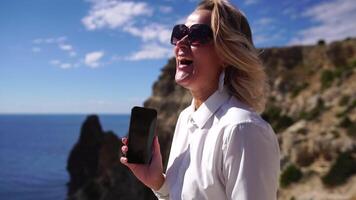 affaires femme parlant par téléphone sur le mer. numérique nomade, jolie Dame dactylographie sur ordinateur par le mer à coucher de soleil, fait du une affaires transaction en ligne de une distance. free-lance, éloigné travail sur vacances video