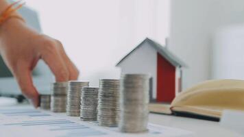 Real estate concept background. House model and coins stack on wooden table, copy space. video