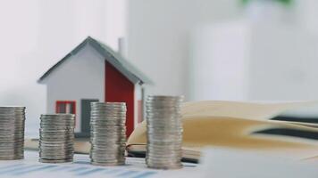 Real estate concept background. House model and coins stack on wooden table, copy space. video