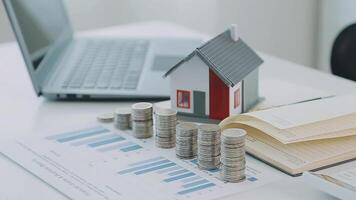 Real estate concept background. House model and coins stack on wooden table, copy space. video