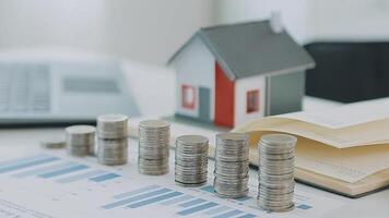 Real estate concept background. House model and coins stack on wooden table, copy space. video