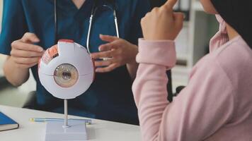 close up of asian female doctor wearing face mask is showing eyeball model and explaining about eyes disease to elder senior man patient in hospital video