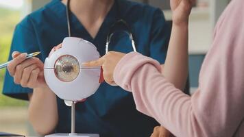 close up of asian female doctor wearing face mask is showing eyeball model and explaining about eyes disease to elder senior man patient in hospital video