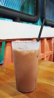A glass of iced chocolate on a wooden table with a straw photo