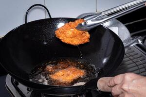 empanizado frito pollo. comidas frito en hirviendo petróleo en un chino wok Cocinando por fritura en caliente aceite. burbujas Aparecer desde fritura foto