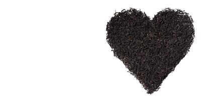 Dry black tea leaves in the shape of heart isolated on white background. Creative banner love for tea. Top view, copy space photo