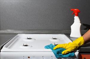 Female hand in glove wiping the panel of gas stove, close-up. Woman washing kitchen apartments, copy space. photo