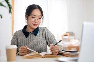 A young Asian female student is focusing on her homework and reading book at a table in her room. photo