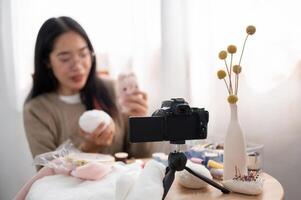 A smiling Asian female content creator is talking with the camera, showing her handmade plushie. photo