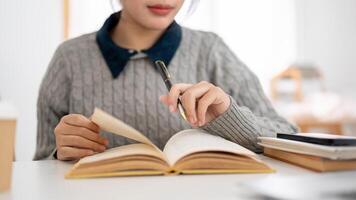 un recortado imagen de un joven asiático hembra estudiante es enfoque en su deberes y leyendo libro. foto