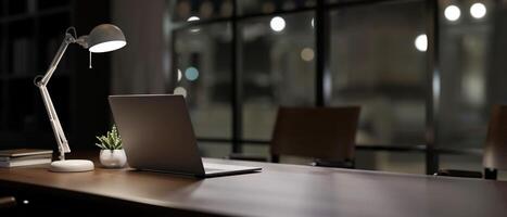 A back view image of a laptop computer on a meeting table in a modern dark meeting room. photo