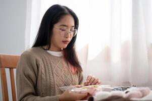 A young Asian woman is focusing on threading a pattern on an embroidery frame, hand sewing on cloth. photo