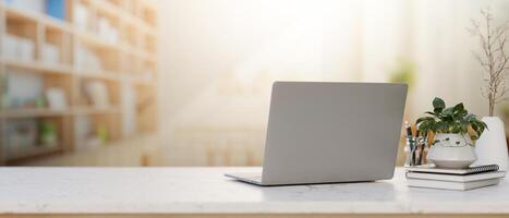 A laptop computer, decor, and space on a white table with a blurred background of a bright library. photo