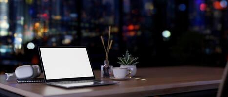 A white-screen laptop computer mockup on a desk in a contemporary office on a skyscraper at night. photo