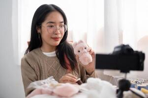 un alegre joven asiático hembra contenido creador demostración su linda hecho a mano peluche a el cámara. foto