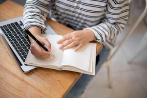A cropped shot of a female student doing homework or taking notes in her notebook at a table. photo