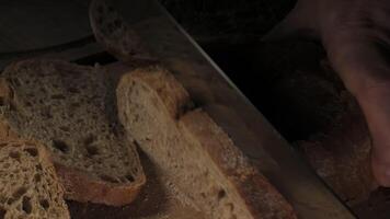 Cutting slice of homemade Crusty rye bread with a sharp knife on wooden board, closeup slow motion video