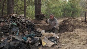 un trabajador borra el bosque de escombros, lanza basura fuera de un agujero sobre un grande pila de basura. seguro ecología concepto. video