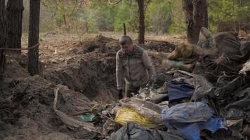 un trabajador borra el bosque de escombros, lanza basura fuera de un agujero sobre un grande pila de basura. seguro ecología concepto. video