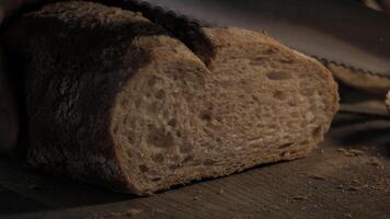 Cutting slice of homemade Crusty rye bread with a sharp knife on wooden board, closeup slow motion video