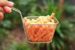 Crispy fried corn sticks in basket on green nature background. photo