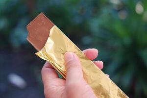 Hand holding a chocolate bar in the garden. Selective focus. photo