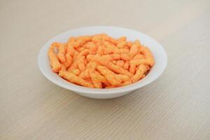 Crispy Corn Puffs in white bowl on wooden background. Selective focus. photo