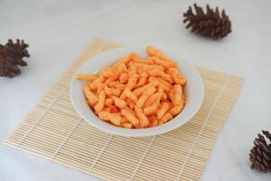 Crispy Corn Puffs in white bowl on bamboo mat photo