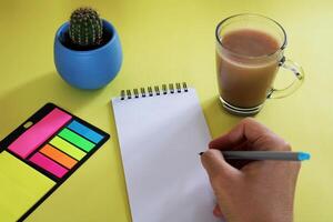 Blank notebook with pen are on top of wood office desk table with a cup of coffee and office supplies, top view. photo