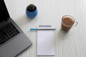 Blank notebook with pen are on top of wood office desk table with a cup of coffee and office supplies, top view. photo