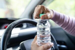 Asian woman driver holding bottle for drink water while driving a car. Plastic hot water bottle cause fire. photo