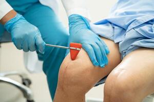 Asian doctor use hammer knock senior woman patient to check knee reflex, nerve and muscle in hospital. photo