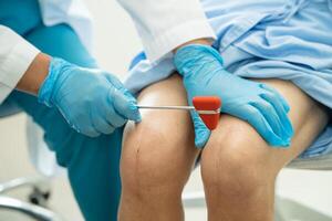 asiático médico utilizar martillo golpe mayor mujer paciente a cheque rodilla reflejo, nervio y músculo en hospital. foto