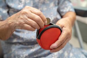 Asian senior woman holding counting coin money in purse. Poverty, saving problem in retirement. photo