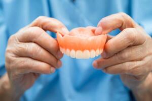 Asian elderly woman patient holding to use denture, healthy strong medical. photo