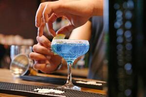 Person Adding Lemon Slice to Cocktail Glass photo