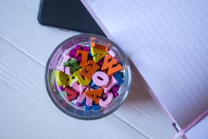 un medio de abrió bloc y multicolor letras en vaso en un blanco de madera escritorio. cerca arriba. foto