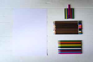 Palette of multicolored pencils and the sheet of white paper on a white wooden desk. photo
