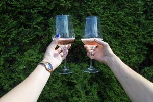 un vaso de vino en De las mujeres manos en contra un natural antecedentes. dos amigos aplausos. Bebiendo vino. foto