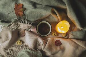A cup of tea, burning candle and fallen leaves on a woolen blanket. Atmospheric autumn background. Cozy autumn. photo