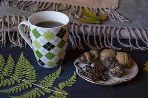 A cup of tea and sweet snacks with decoration by autumn leaves on the blue wooden background. Seasonal still life. photo