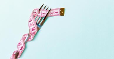 Fork wrapped in measuring tape on blue background. Top view of overeating concept photo