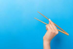 Girl's hand showing chopsticks on blue background. Asian cuisine concept with empty space for your design photo