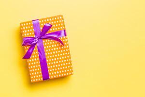 Gift box with purple bow for Christmas or New Year day on yellow background, top view with copy space photo