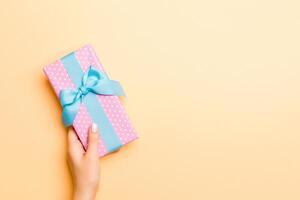 Flat lay of woman hands holding gift wrapped and decorated with bow on gold background with copy space. Christmas and holiday concept photo