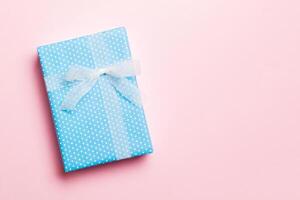 Gift box with white bow in hands for Christmas or New Year day on pink background, top view with copy space photo